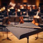 Conductor's baton in front of orchestra instruments.